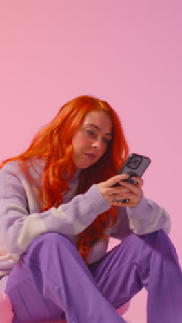 Vertical-Video-Studio-Shot-Of-Young-Gen-Z-Woman-Gaming-Streaming-Or-Using-Social-Media-On-Mobile-Phone-Against-Pink-Background